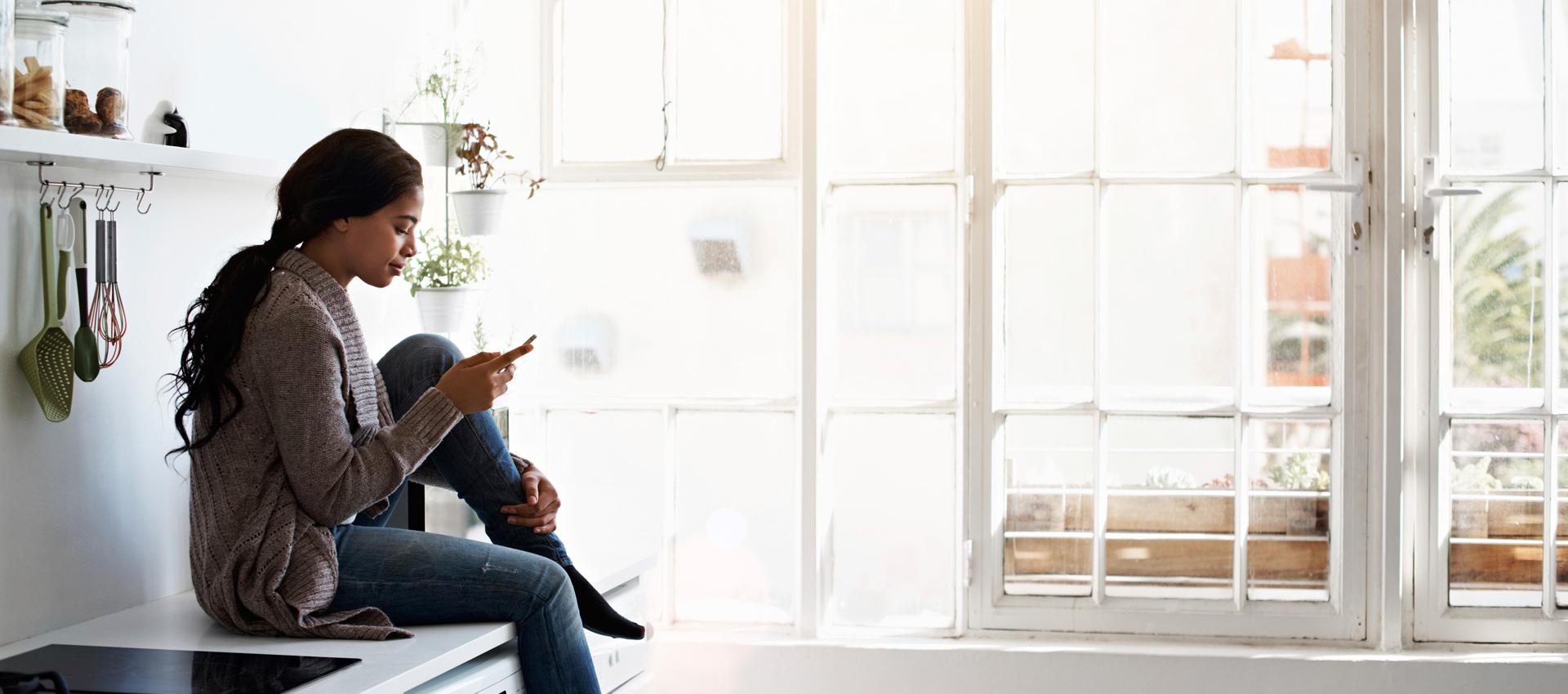 Woman sitting on the counter in the kitchen, on her phone.