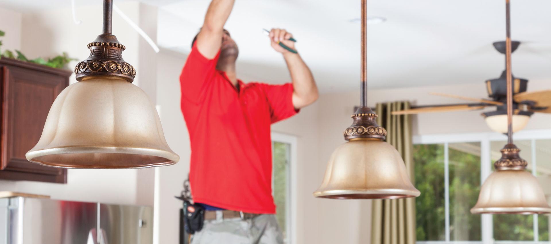 A service technician working on pendant lights over an island in the kitchen.