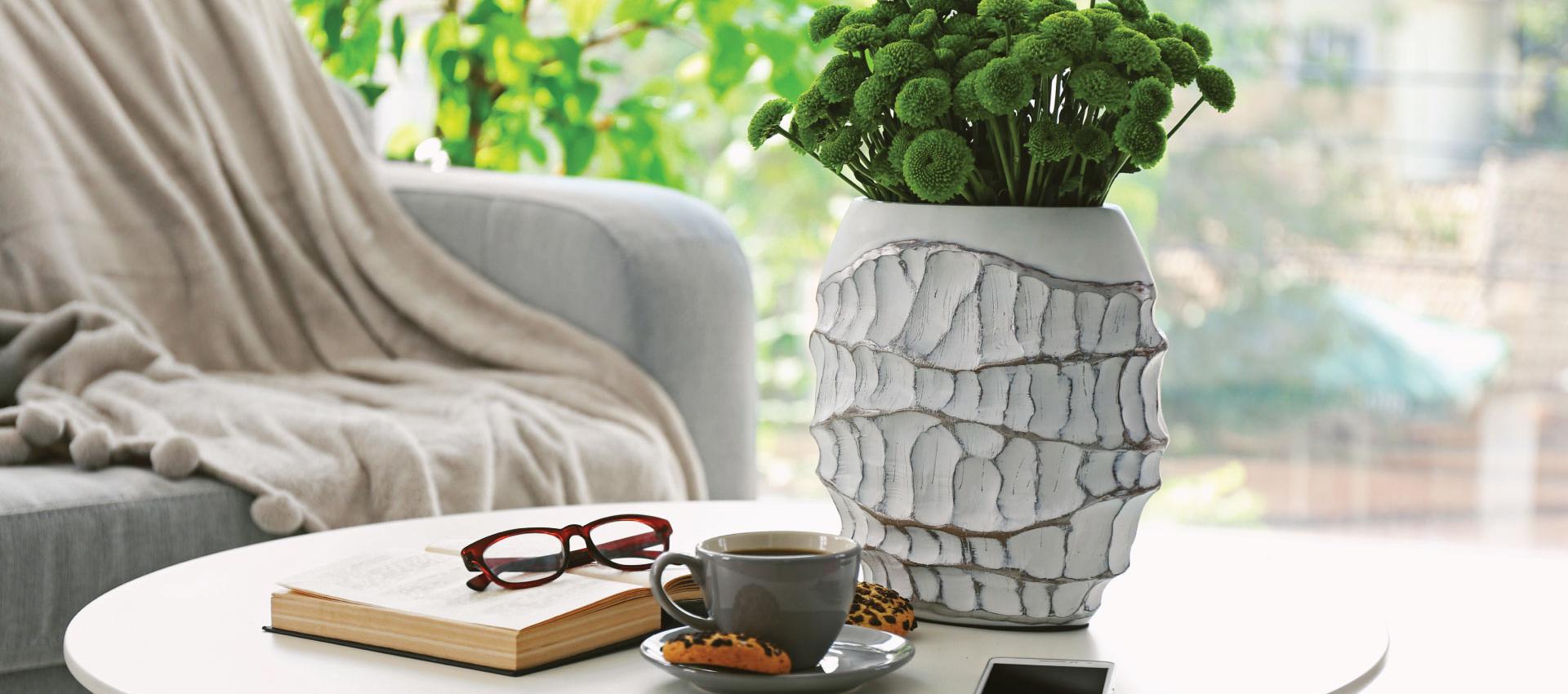 A coffee table with a book, a cup of coffee, plant and reading glasses.