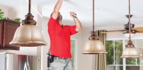 A service technician working on pendant lights over an island in the kitchen.